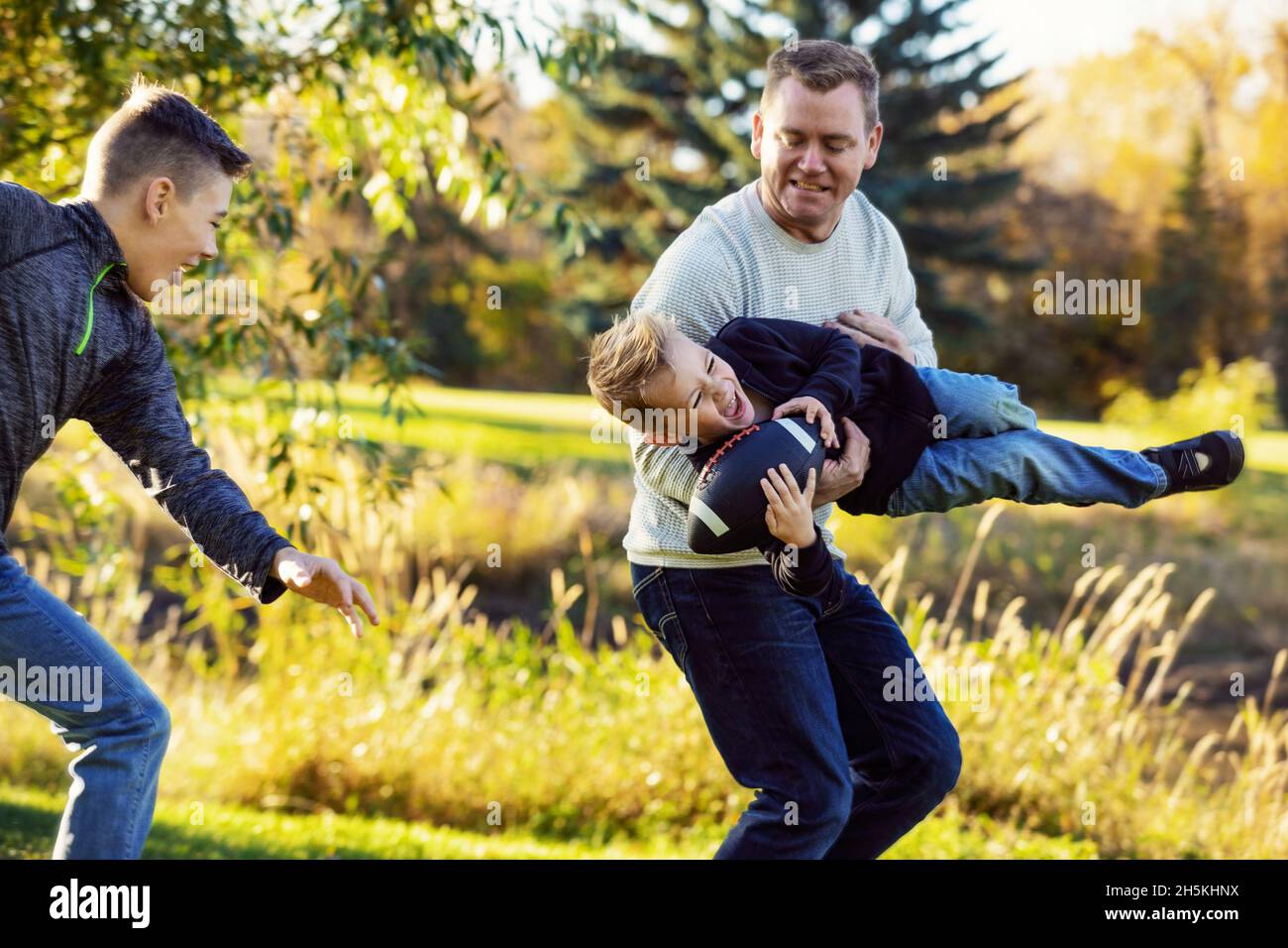 Father playing with his two sons in a park in autumn; St. Albert, Alberta, Canada Stock Photo