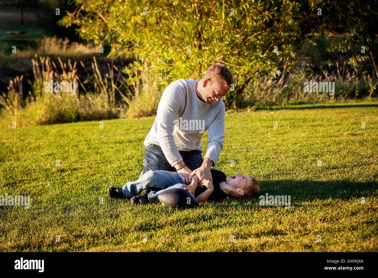 Father and young son roughhousing on the grass in a city park; St. Albert, Alberta, Canada Stock Photo