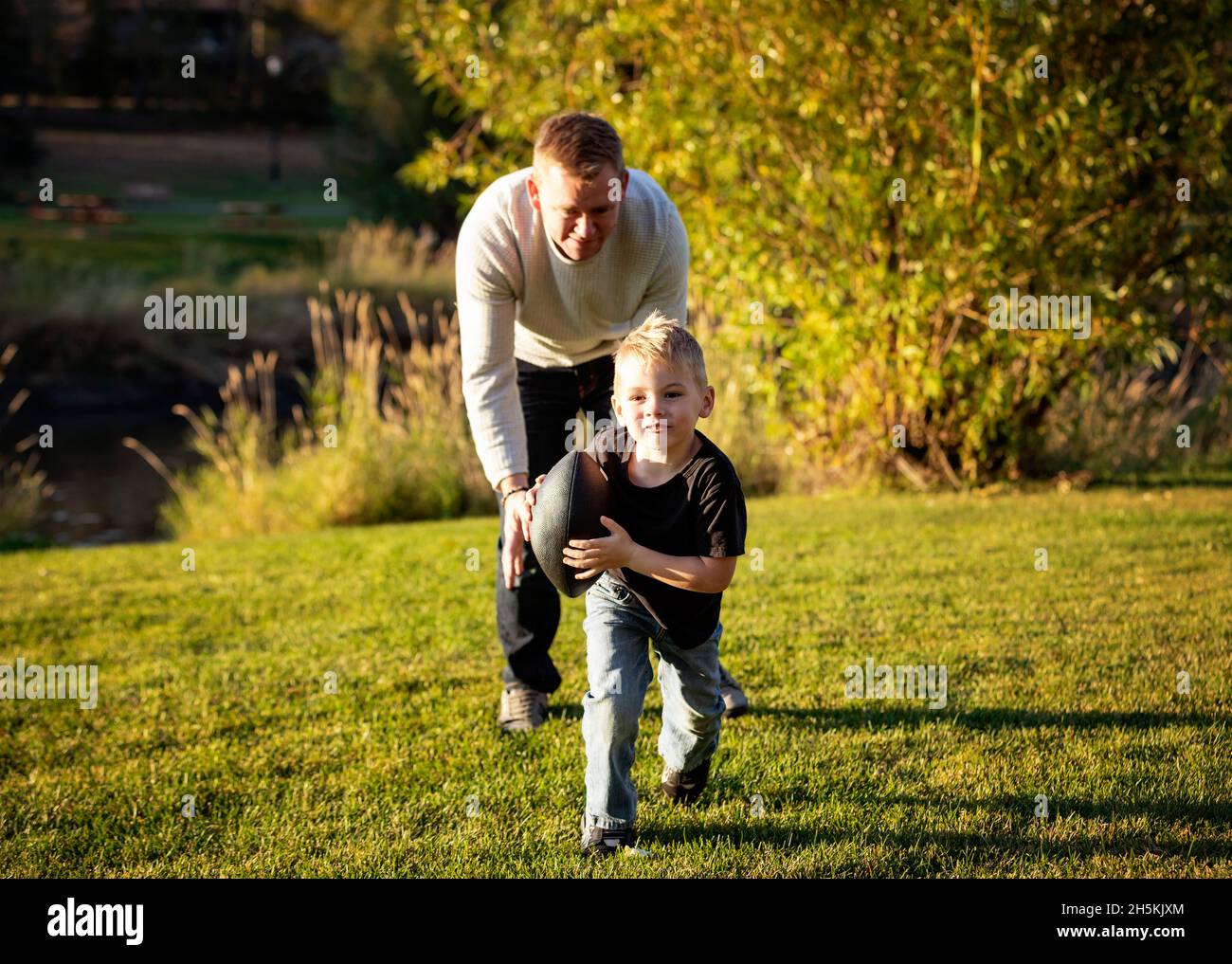 Father playing football with his young son in a park in autumn; St. Albert, Alberta, Canada Stock Photo