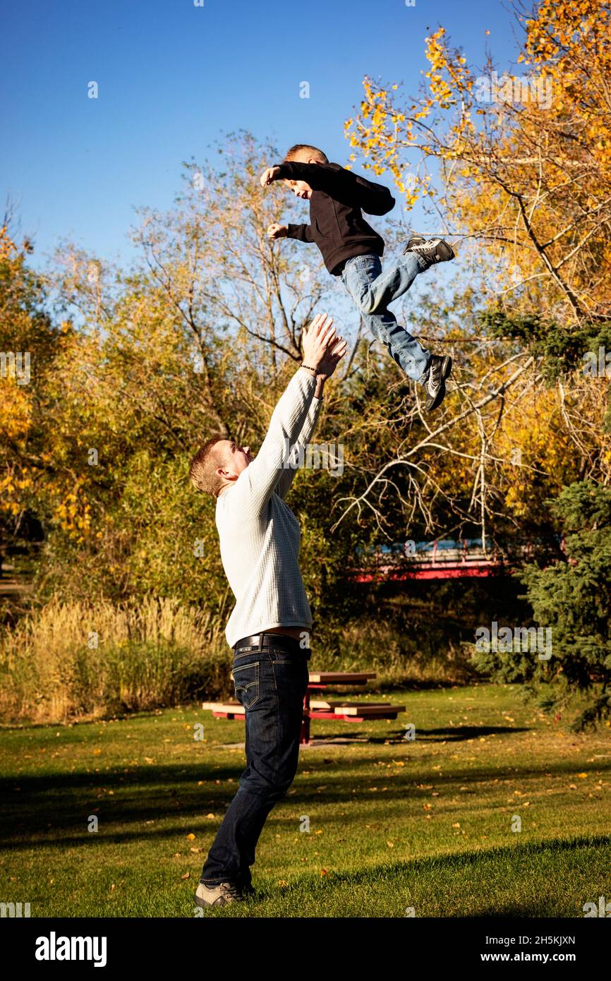 Father playing with his young son in a park in autumn, tossing him high in the air; St. Albert, Alberta, Canada Stock Photo