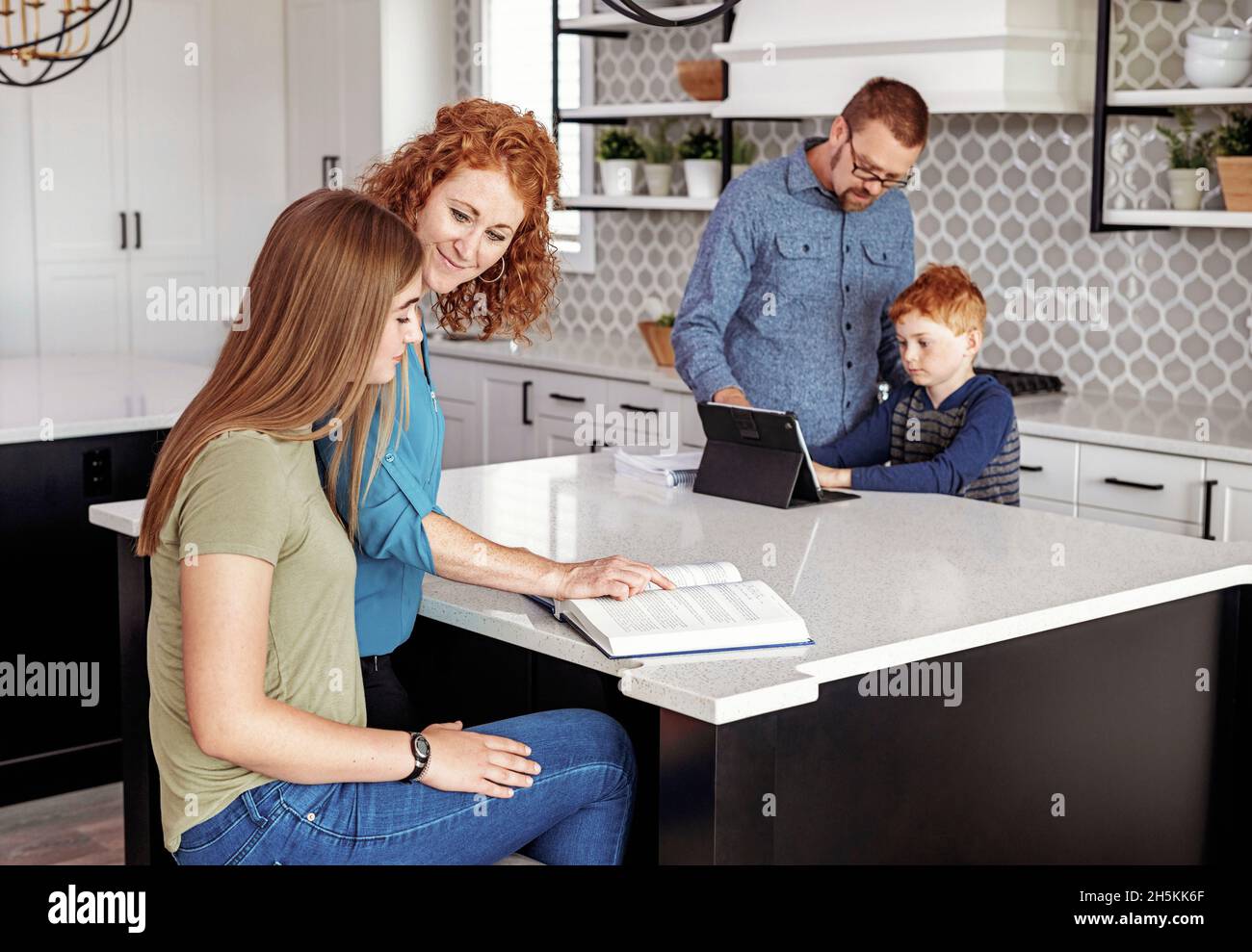 Parents helping young son and teenage daughter with homework in the home kitchen; Edmonton, Alberta, Canada Stock Photo