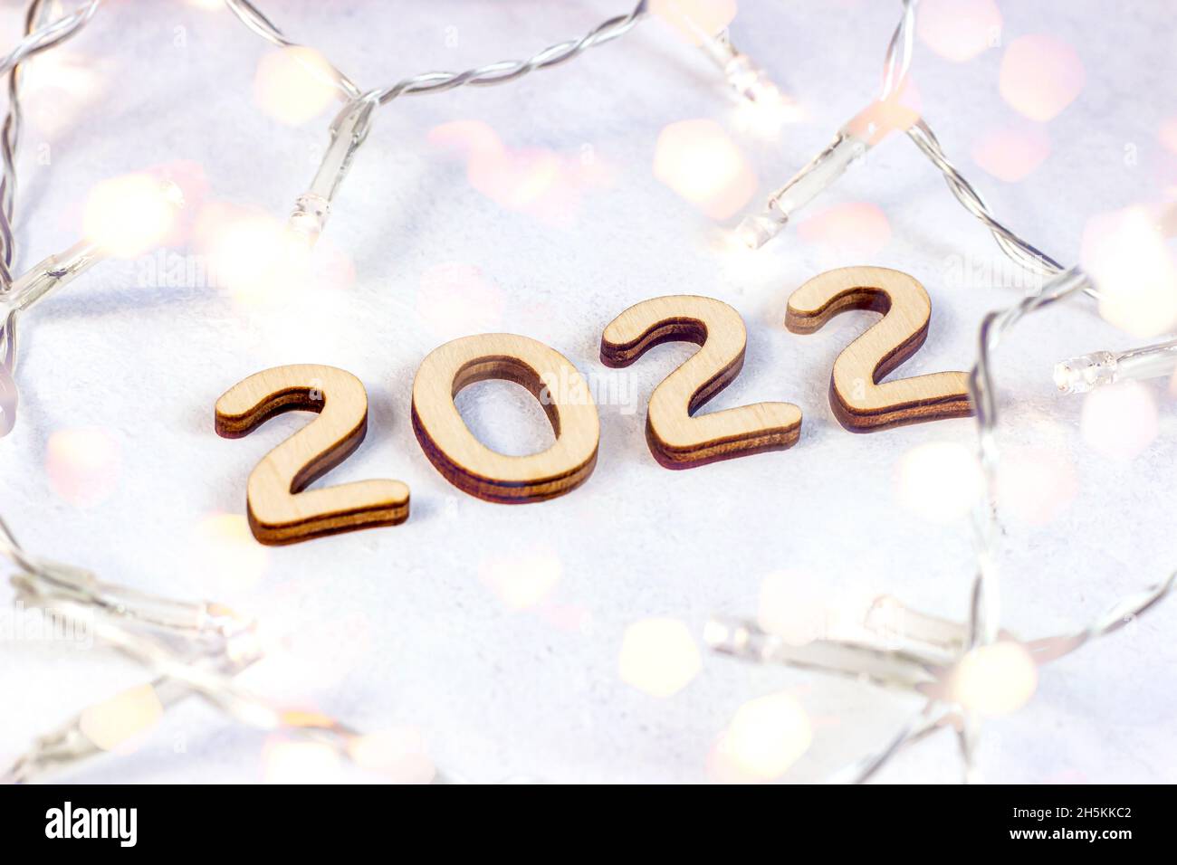 Wooden numbers 2022 silhouette with Christmas lights on light background. New Year beginning congratulations and planning concept. Stock Photo