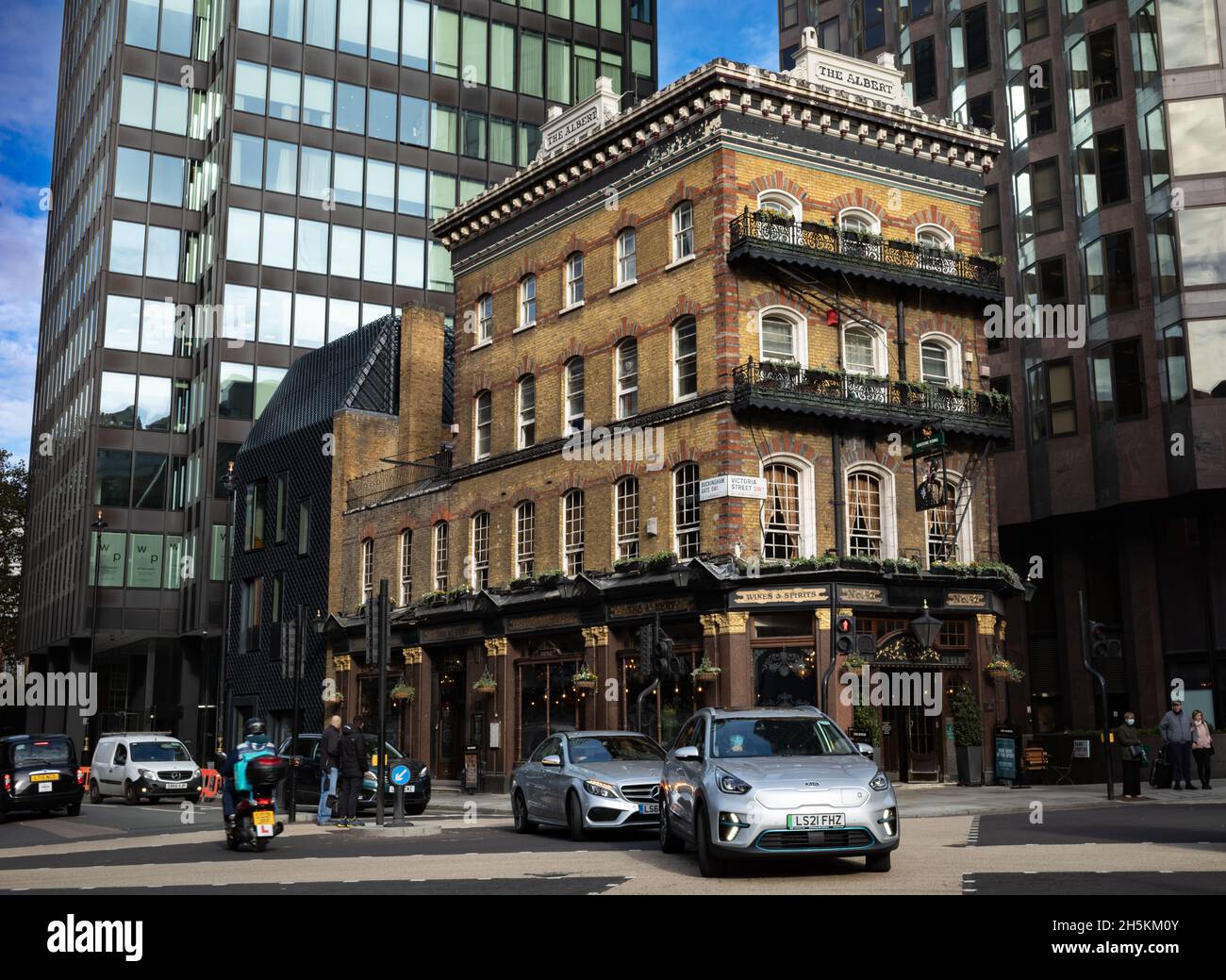 An electric car passes in front of the the landmark Albert pub in Victoria St, London, an old pub surrounded by modern buildings. Electric vehicles ar Stock Photo