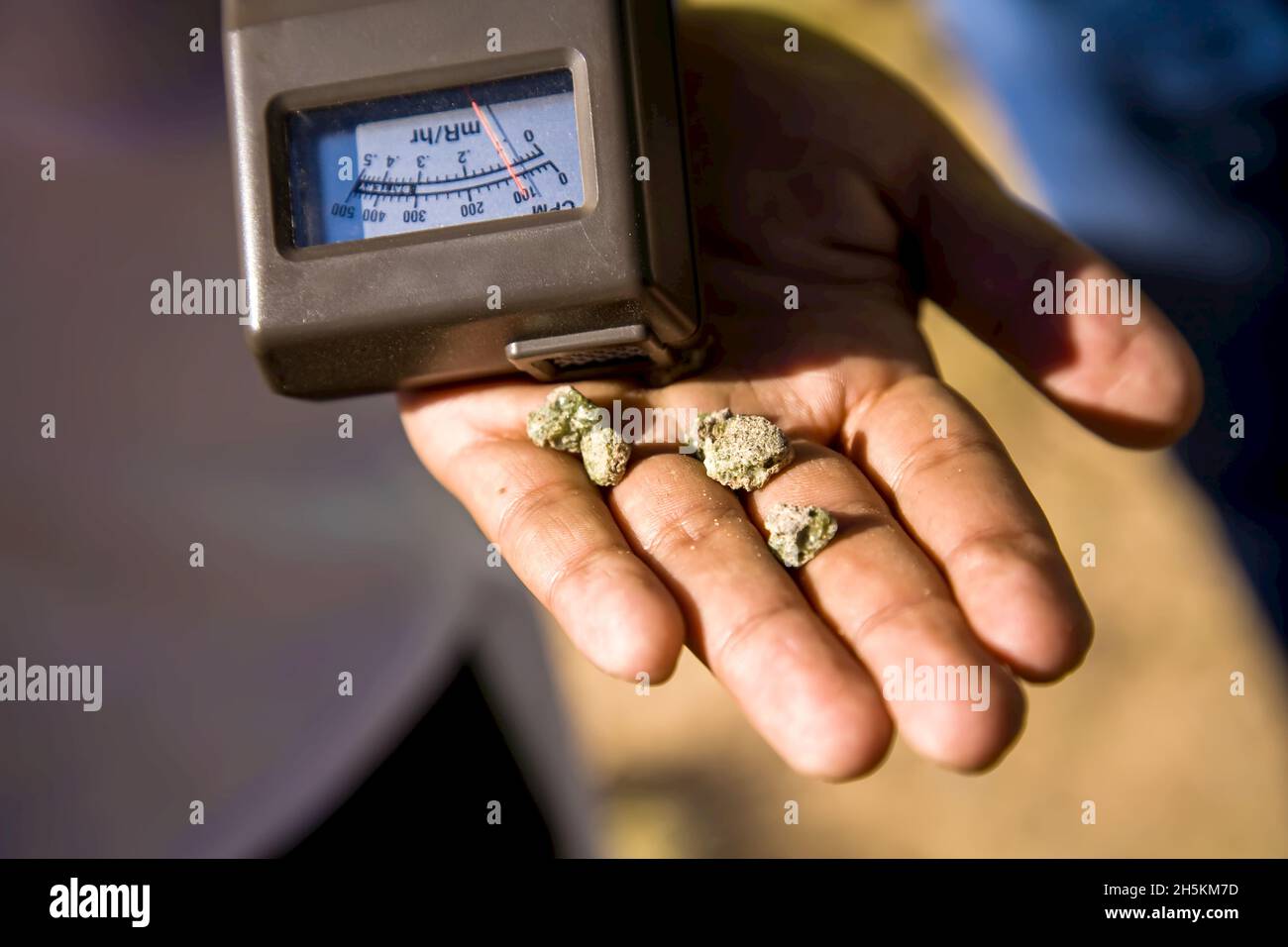Geiger counter and trinitite in a human hand. Stock Photo