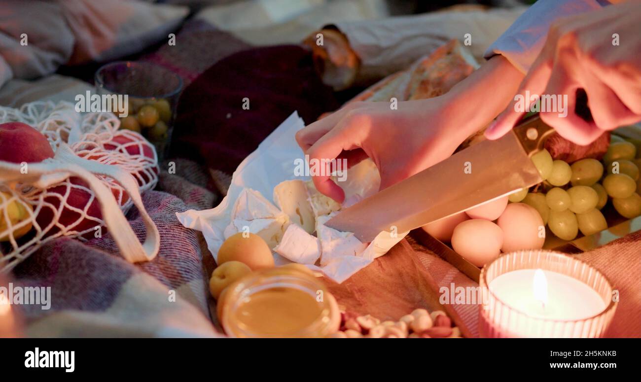 A woman is cutting cheese during a night picnic Stock Photo