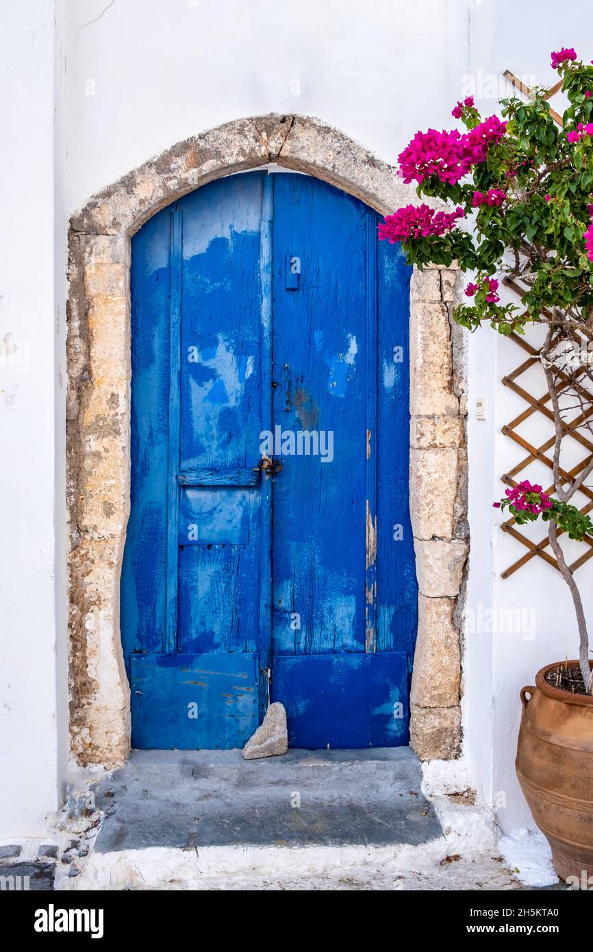 Greek island typical architecture. Kythira Chora town, Greece. Blue wooden door and red bougainvillea on whitewashed house wall. Sunny summer day Stock Photo