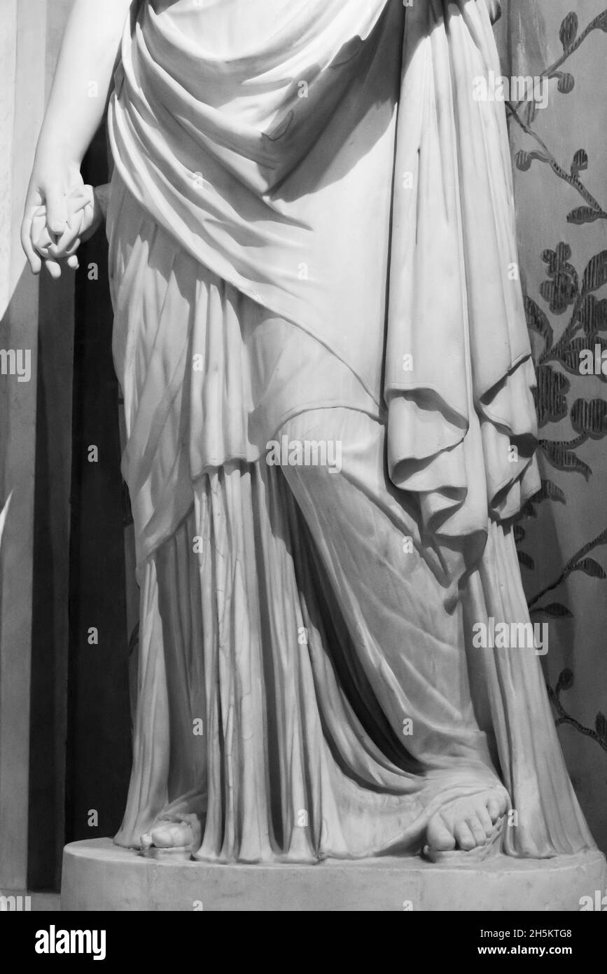 Black and white photo showing in detail the lower part of ancient roman statue sculpted in marble representing a woman wearing a long tunic Stock Photo