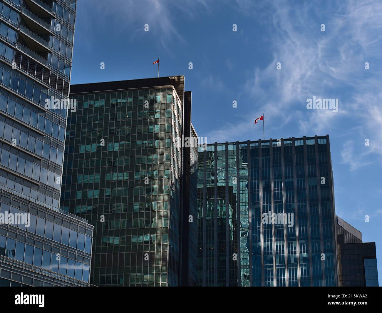 Low angle view of modern high-rise office buildings with glass facades and waving Canadian national flags in district Coal Harbour in Vancouver. Stock Photo