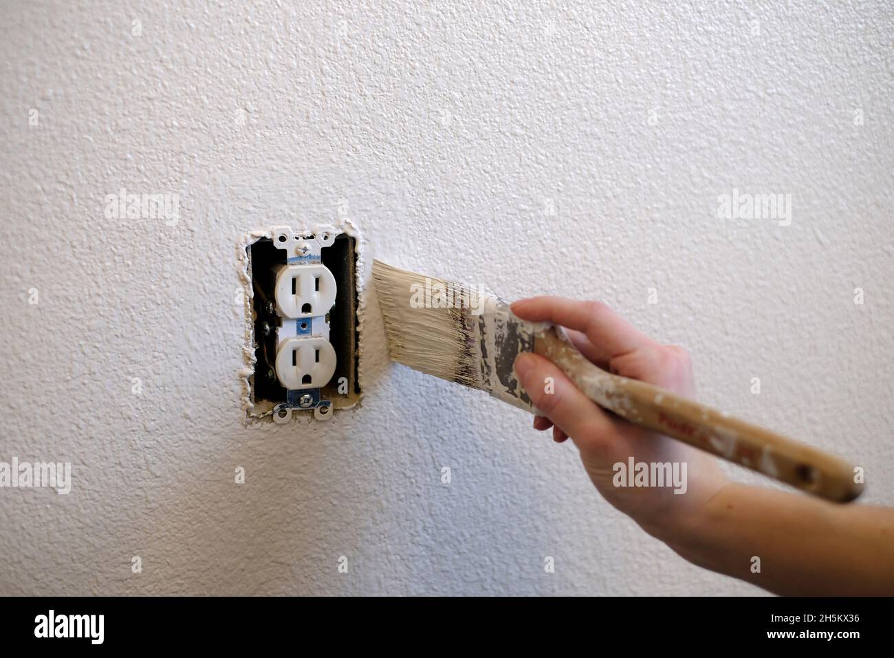 Person hand painting around electrical outlet with paintbrush white