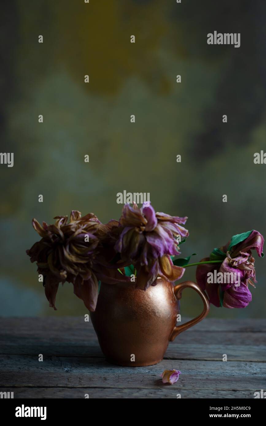 still life of wilted flowers in a copper vase, on a wooden table