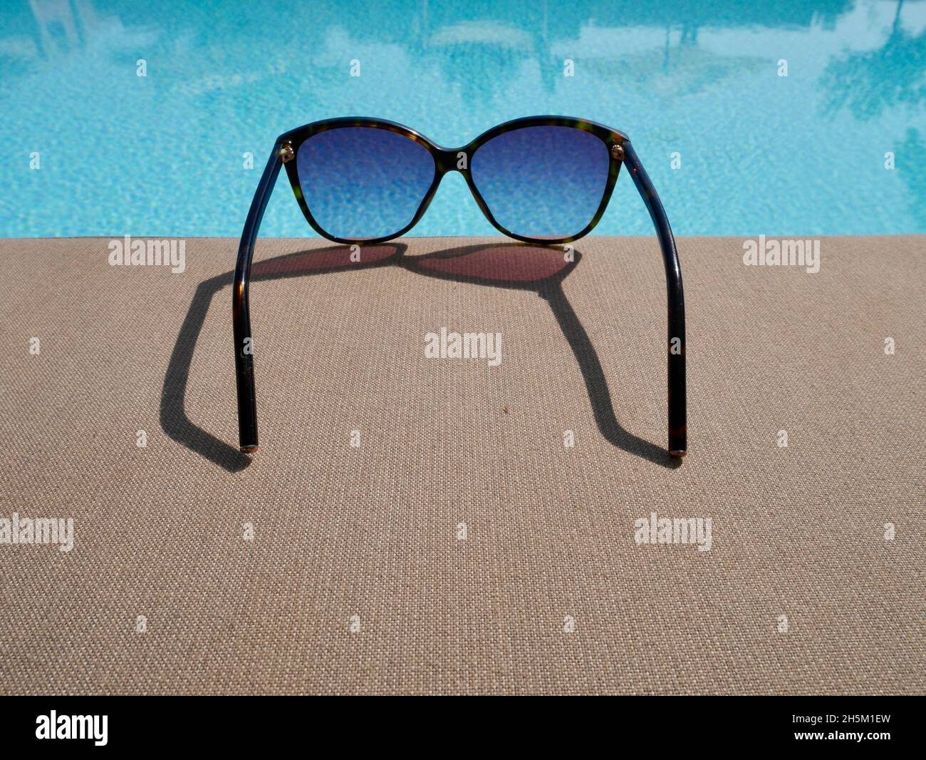 Close up of sunglasses laying besides pool. Summer time background, holidays, travel concept. Stock Photo