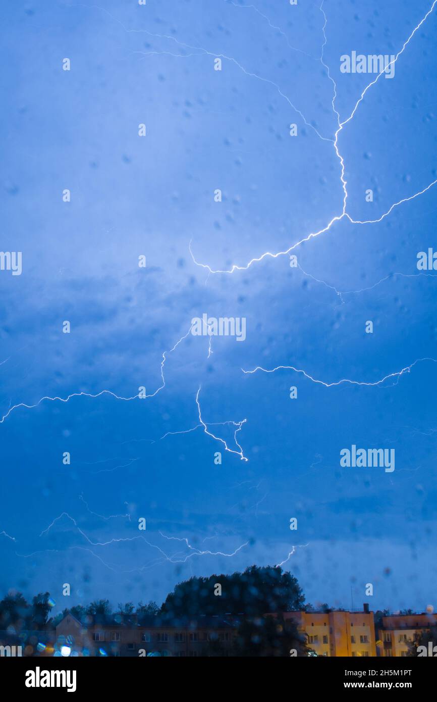 Lightning bolts striking in the dark cloudy night sky through a wet ...