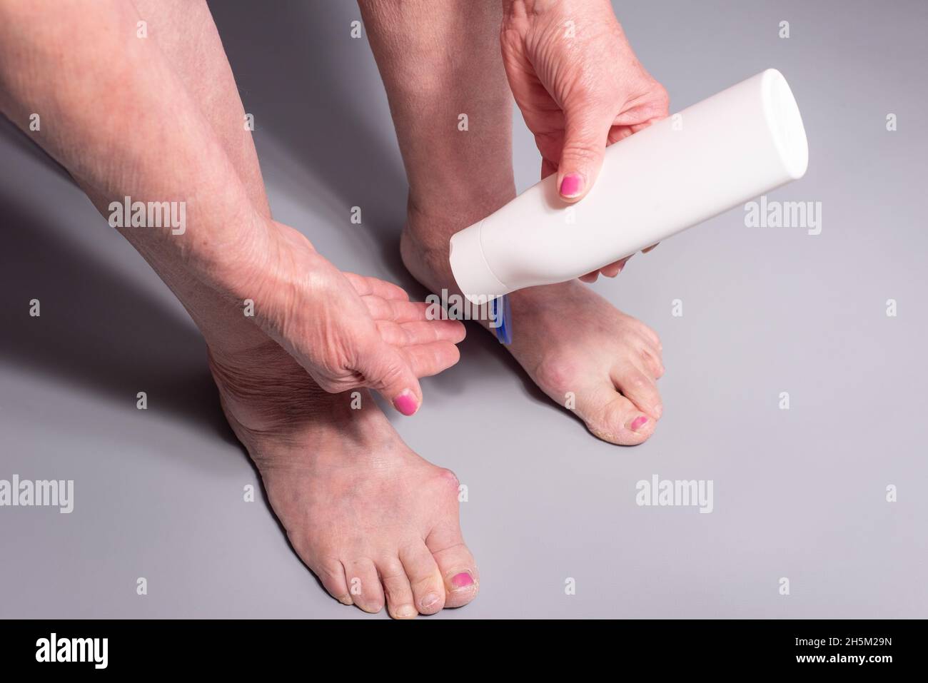 foot cream old woman applying cream from a tube to feet on a gray background Stock Photo