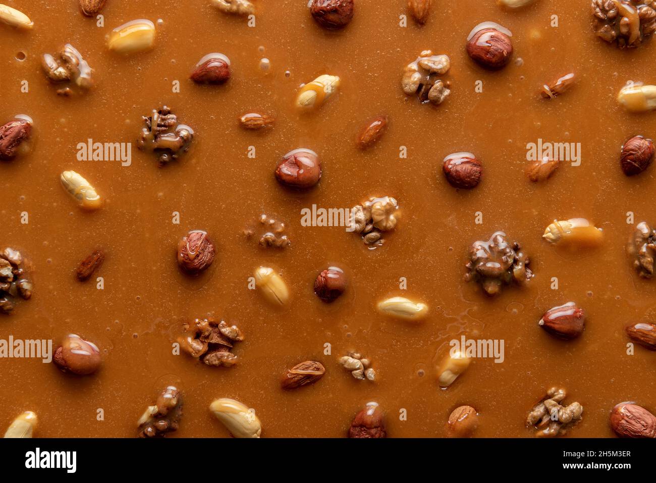 Melted caramel sauce with assorted nuts, full-frame image. Top view of peanut brittle ingredients. Caramelized hazelnuts and peanuts in caramel syrup Stock Photo