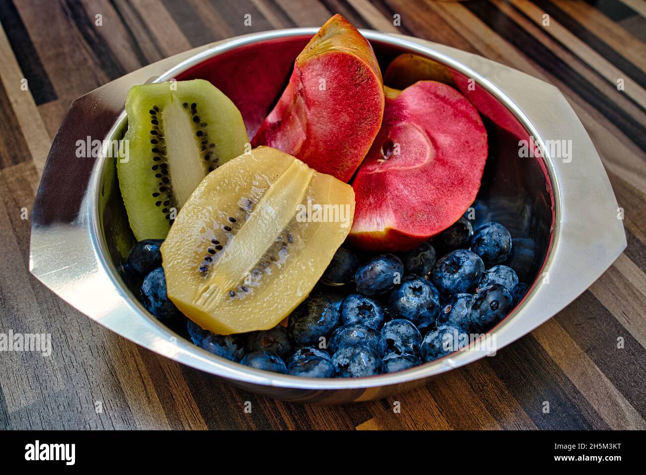 halved green and kiwis, blueberries and an apple called red moon in a stainless steel on a table Photo - Alamy