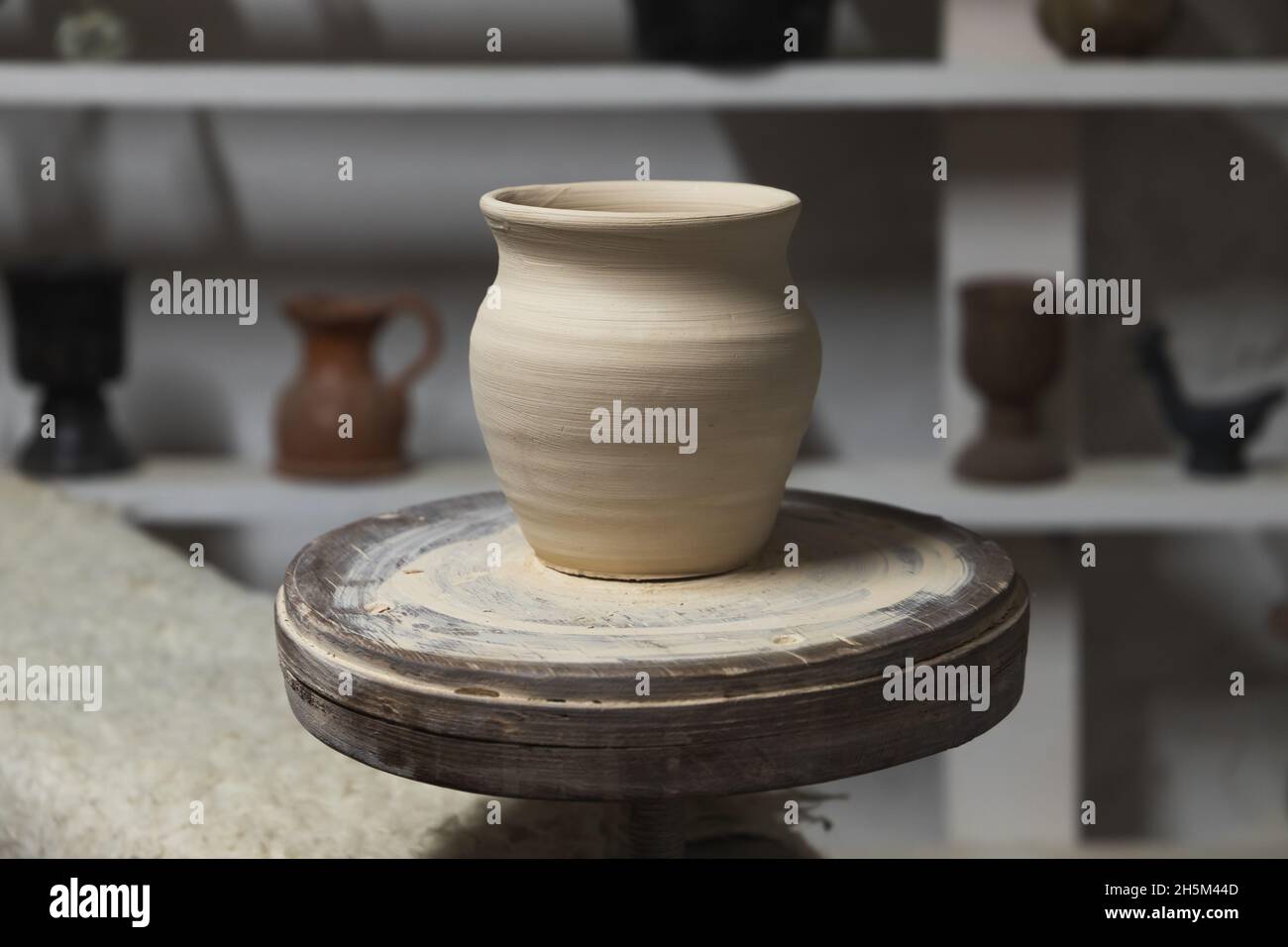 White clay pot stands on a pottery wheel in a workshop studio, close up photo Stock Photo