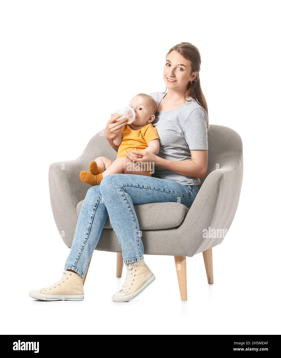 Young mother feeding little baby in armchair on white background Stock