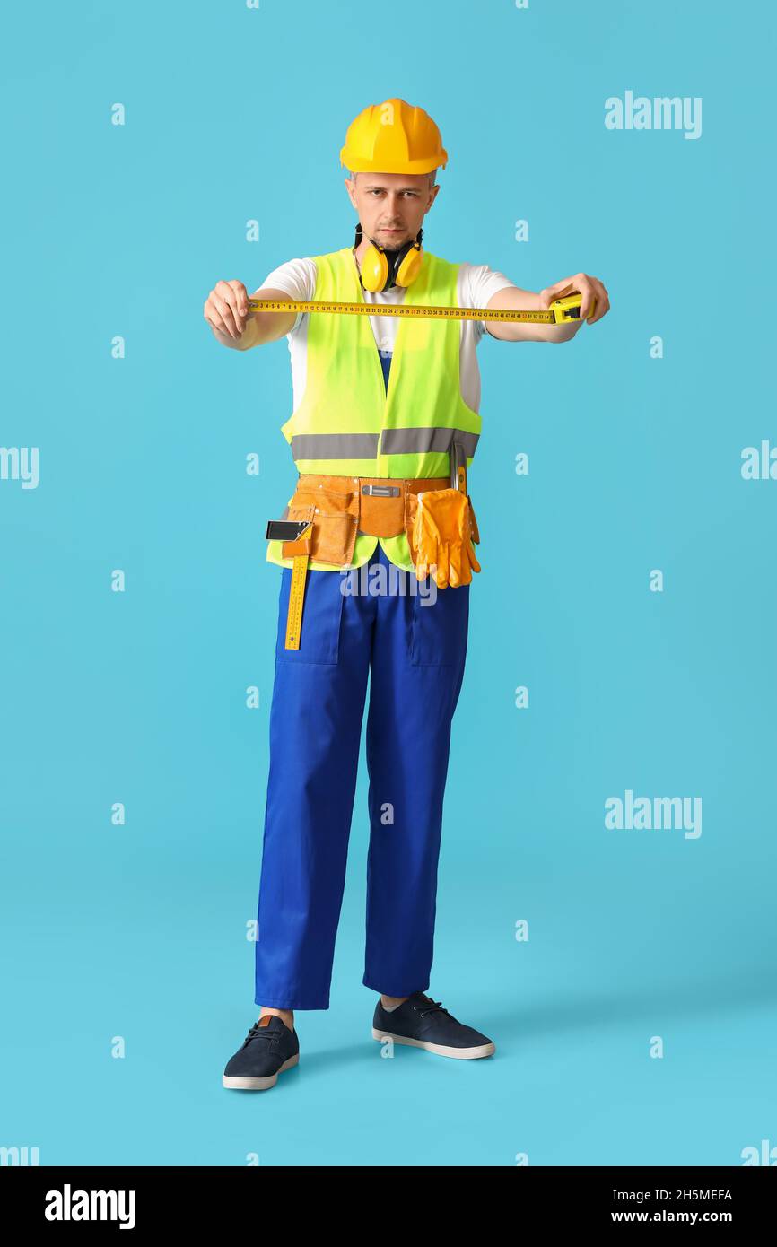 Male builder with tape measure on color background Stock Photo