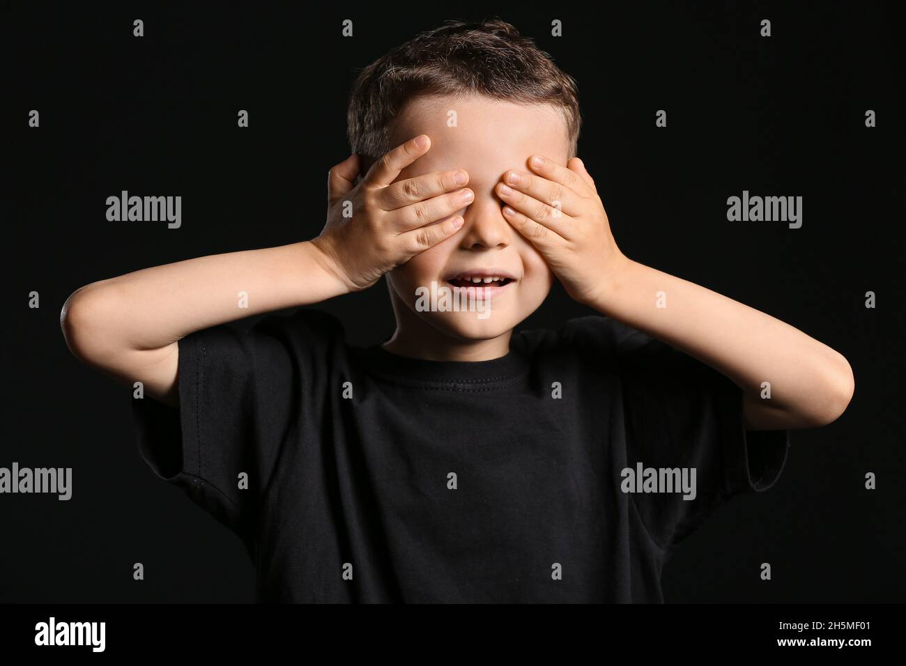 Portrait of cute little boy covering eyes with his hands on dark ...