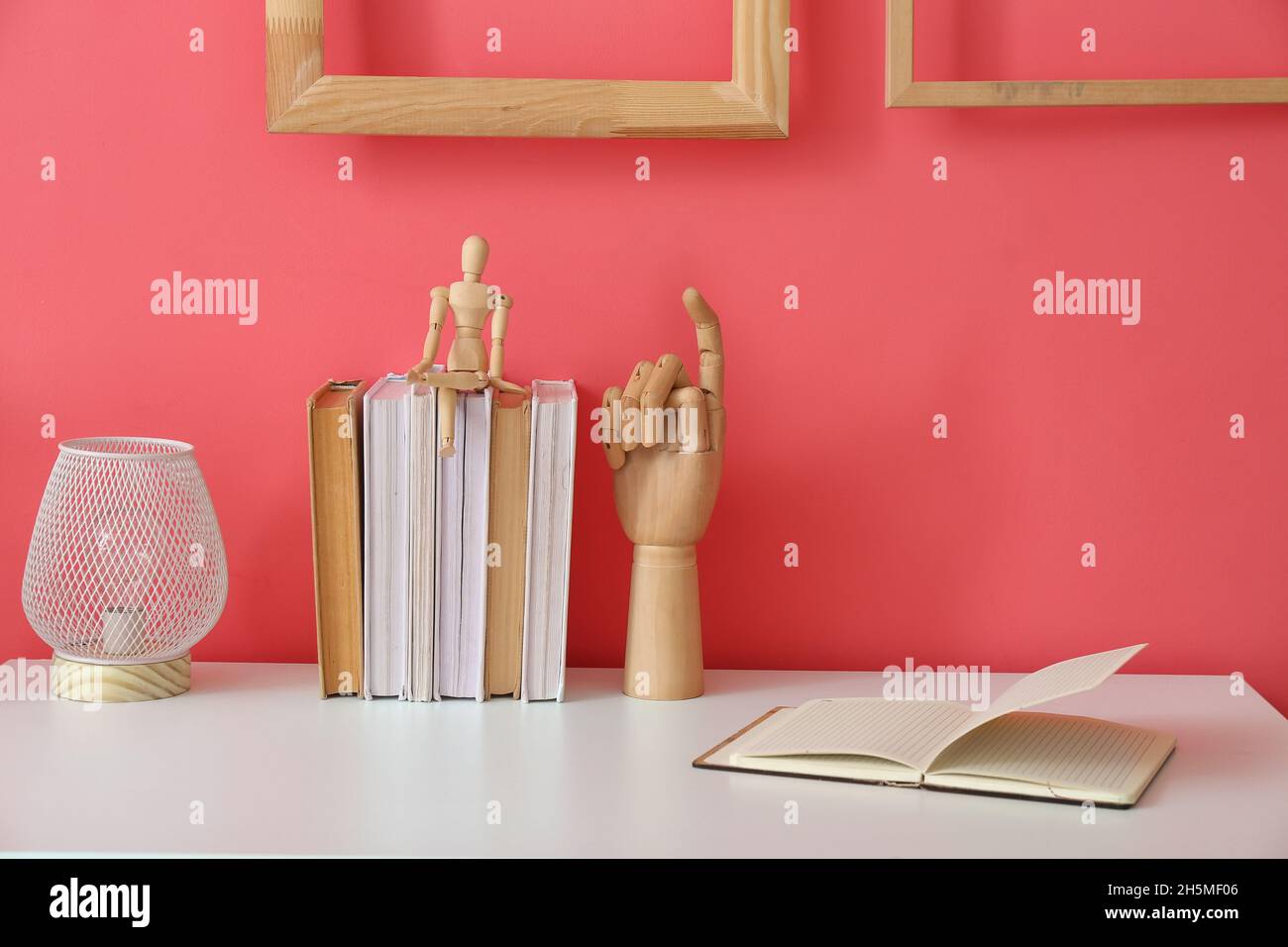 Modern lamp, wooden hand, puppet and books on white table near color ...