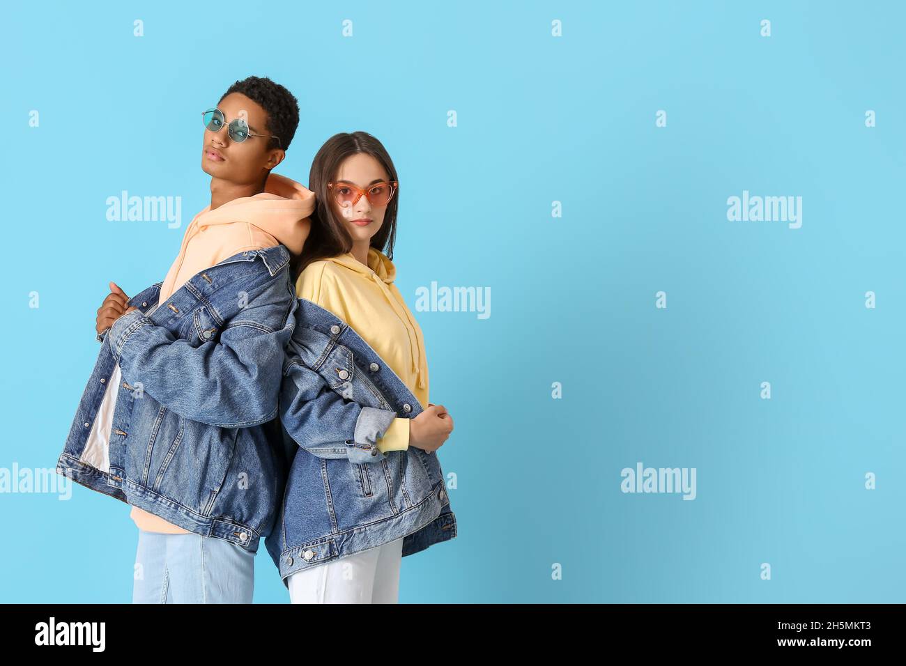 Stylish young couple in hoodies and denim jackets on blue background Stock Photo