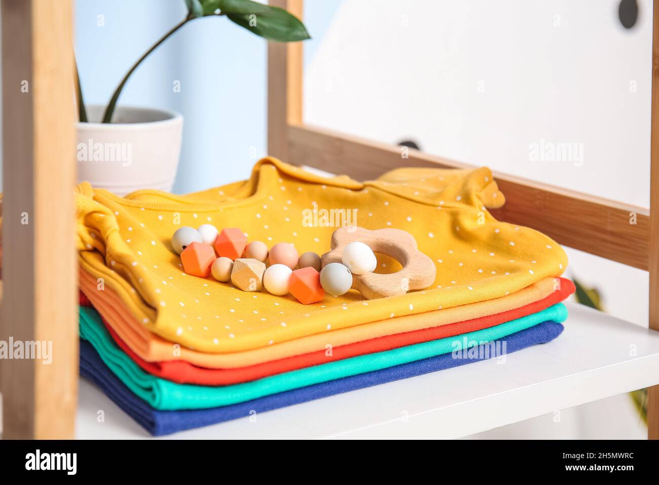 Stack of baby clothes and toy on shelf near color wall Stock Photo - Alamy