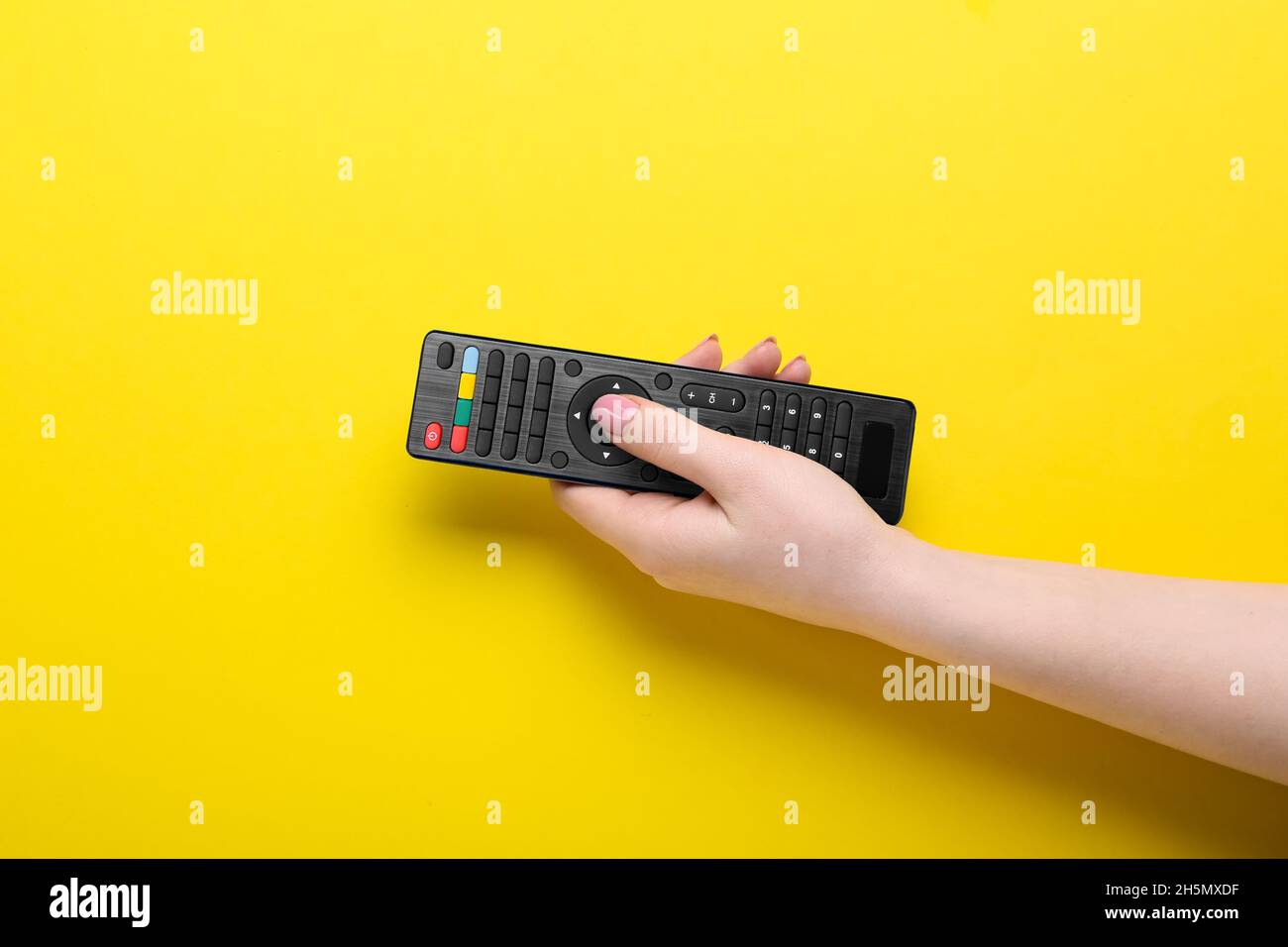 Woman pressing button on TV remote controller on yellow background Stock Photo