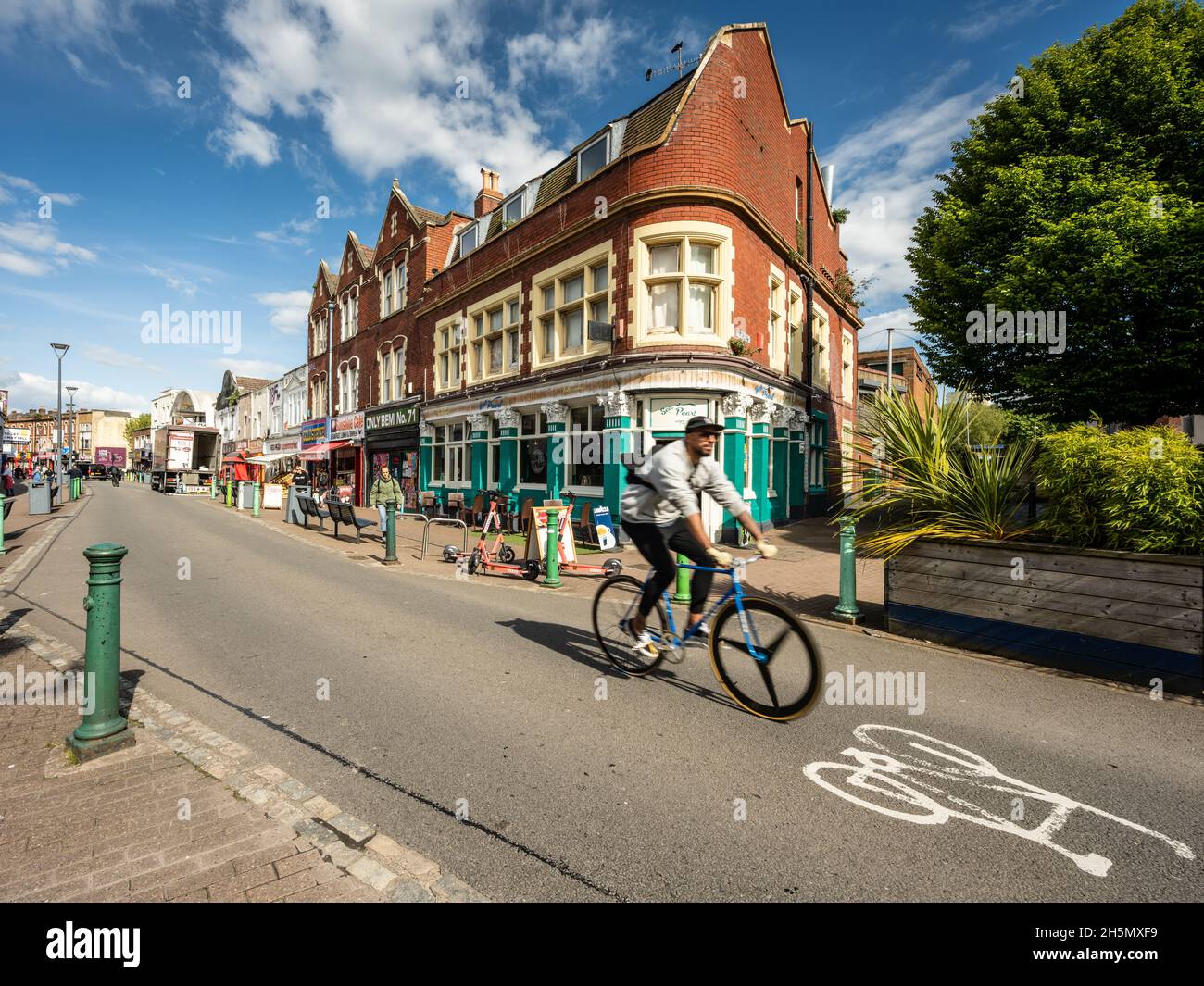 Cyclists and pedestrians pass independent shops, cafes and restaurants on East Street in Bedminster, Bristol. Stock Photo
