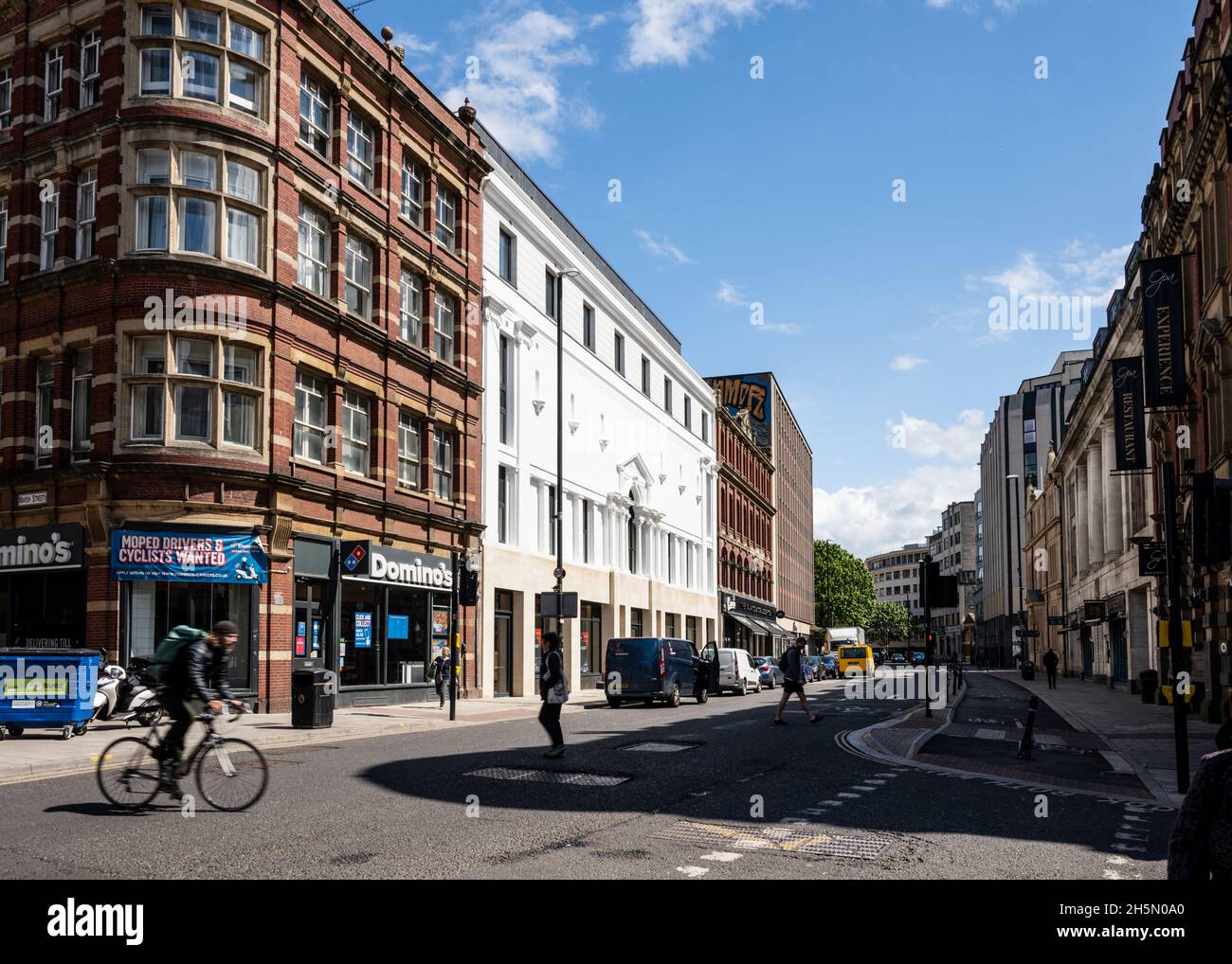 Cyclists and pedestrians pass shops, offices and apartment buildings on Baldwin Street in Bristol city centre. Stock Photo