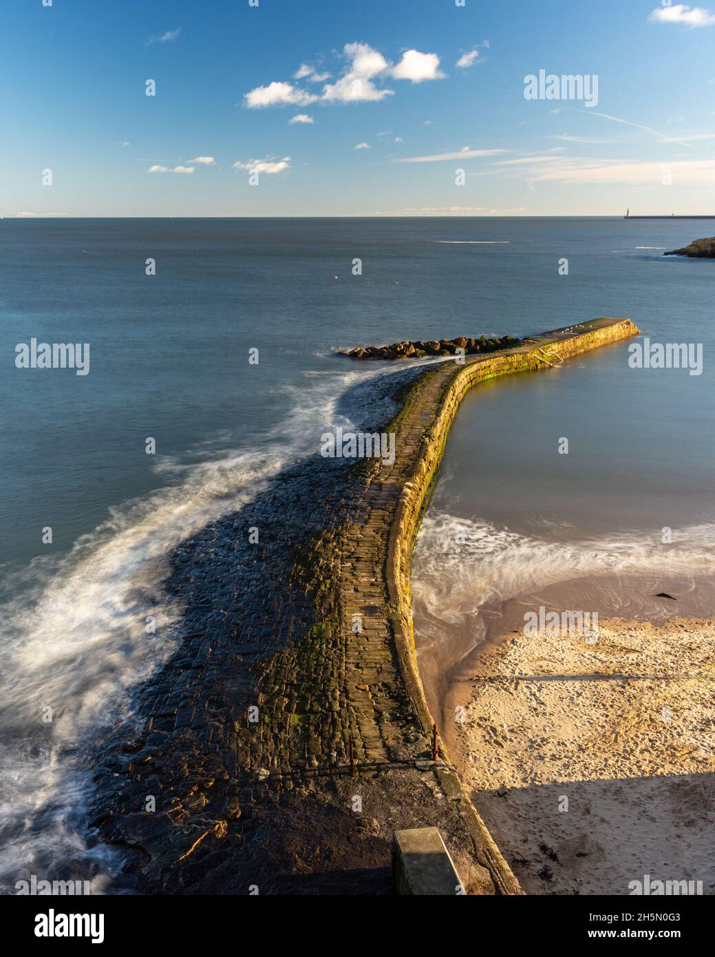 Waves break on the stone harbour wall of Cullercoats Bay on Tyneside's North Sea Coast. Stock Photo