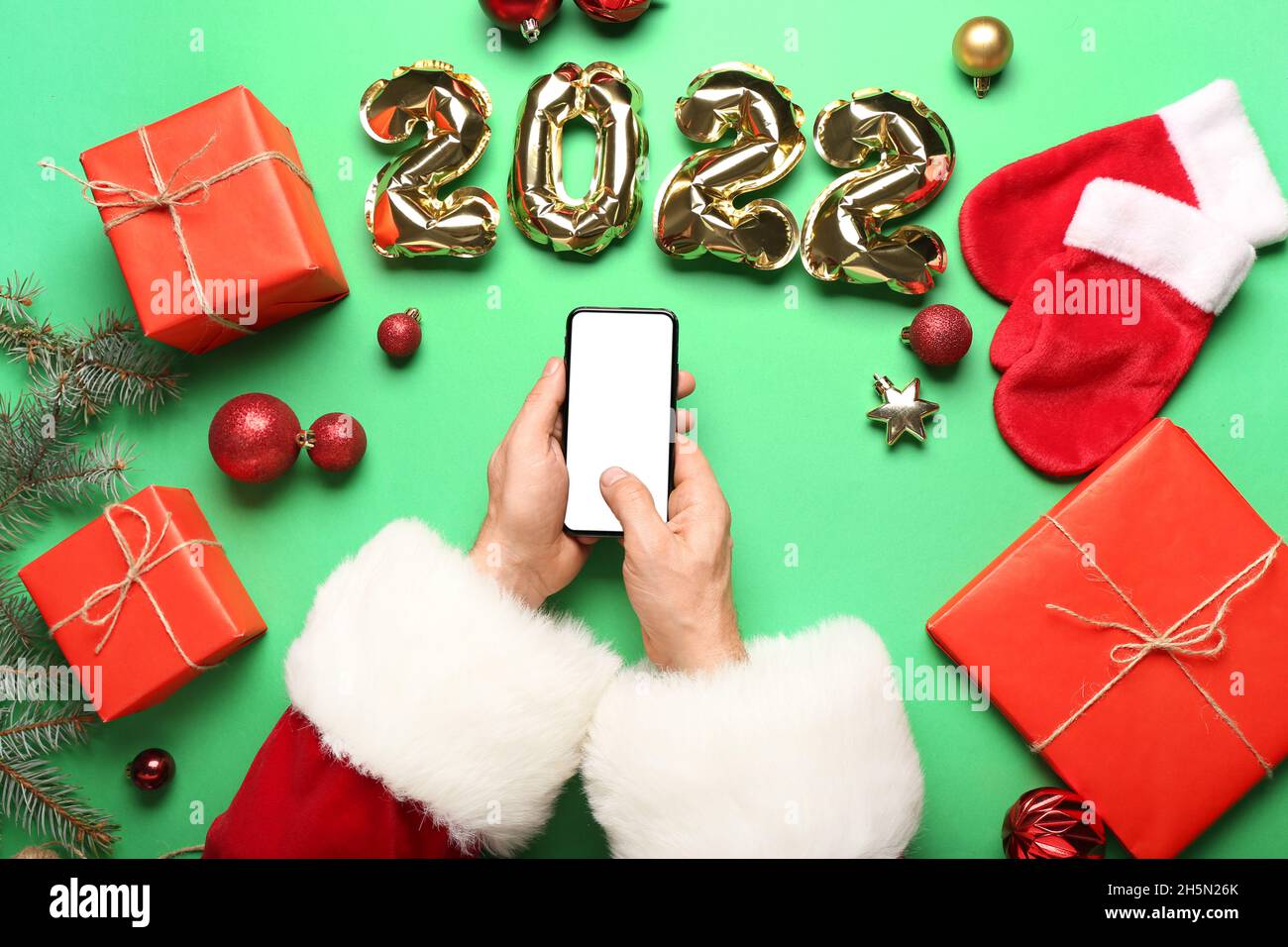 Santa Claus with mobile phone and balloons in shape of figure 2022 on green background Stock Photo