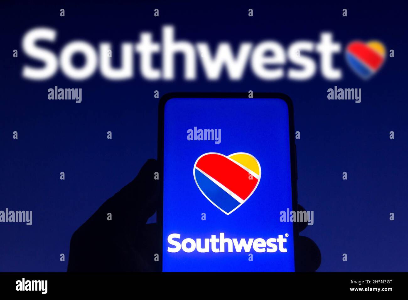 In this photo illustration the Southwest Airlines logo seen displayed on a smartphone screen and in the background. Stock Photo