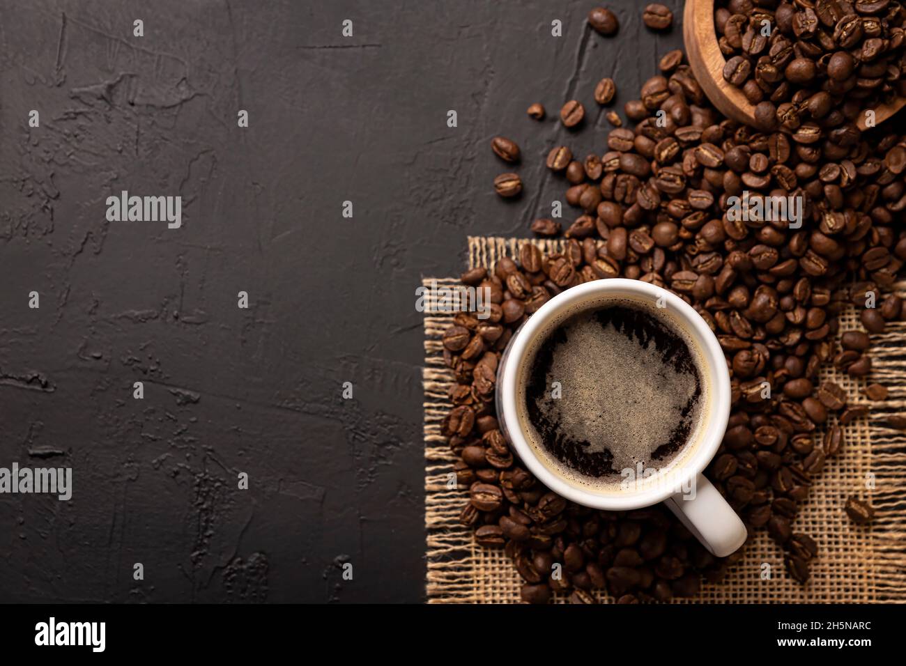White lungo cup with hot coffee drink and toasted coffee beans scattered on a rustic black table. Top view with Copy space for your text Stock Photo