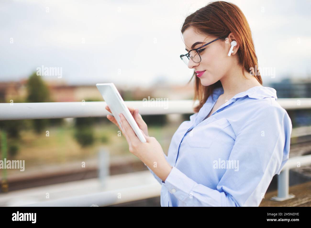 Redhead Caucasian young businesswoman with hands-free device using tablet outdoors Stock Photo