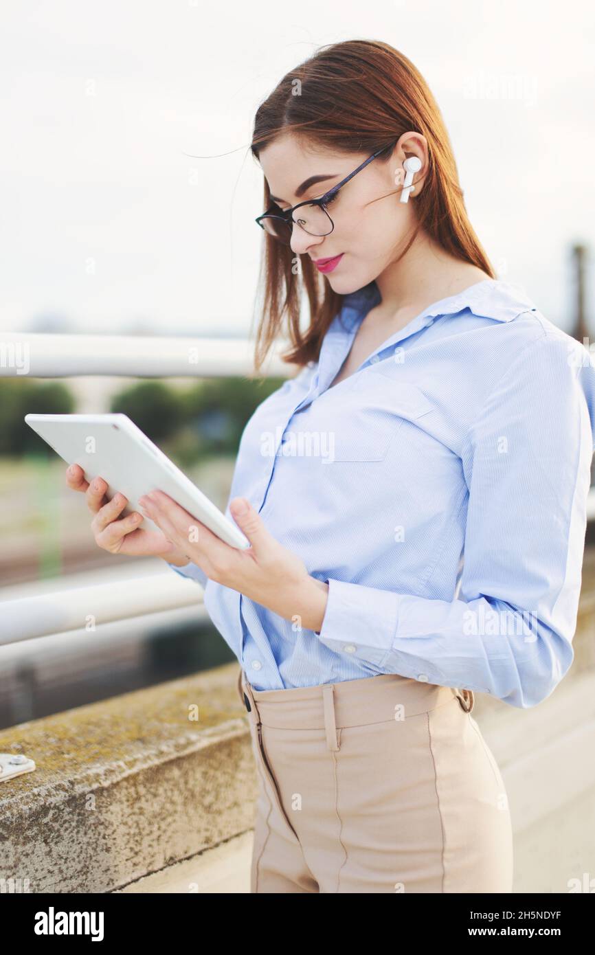 Redhead Caucasian young businesswoman with hands free device using tablet outdoors Stock Photo