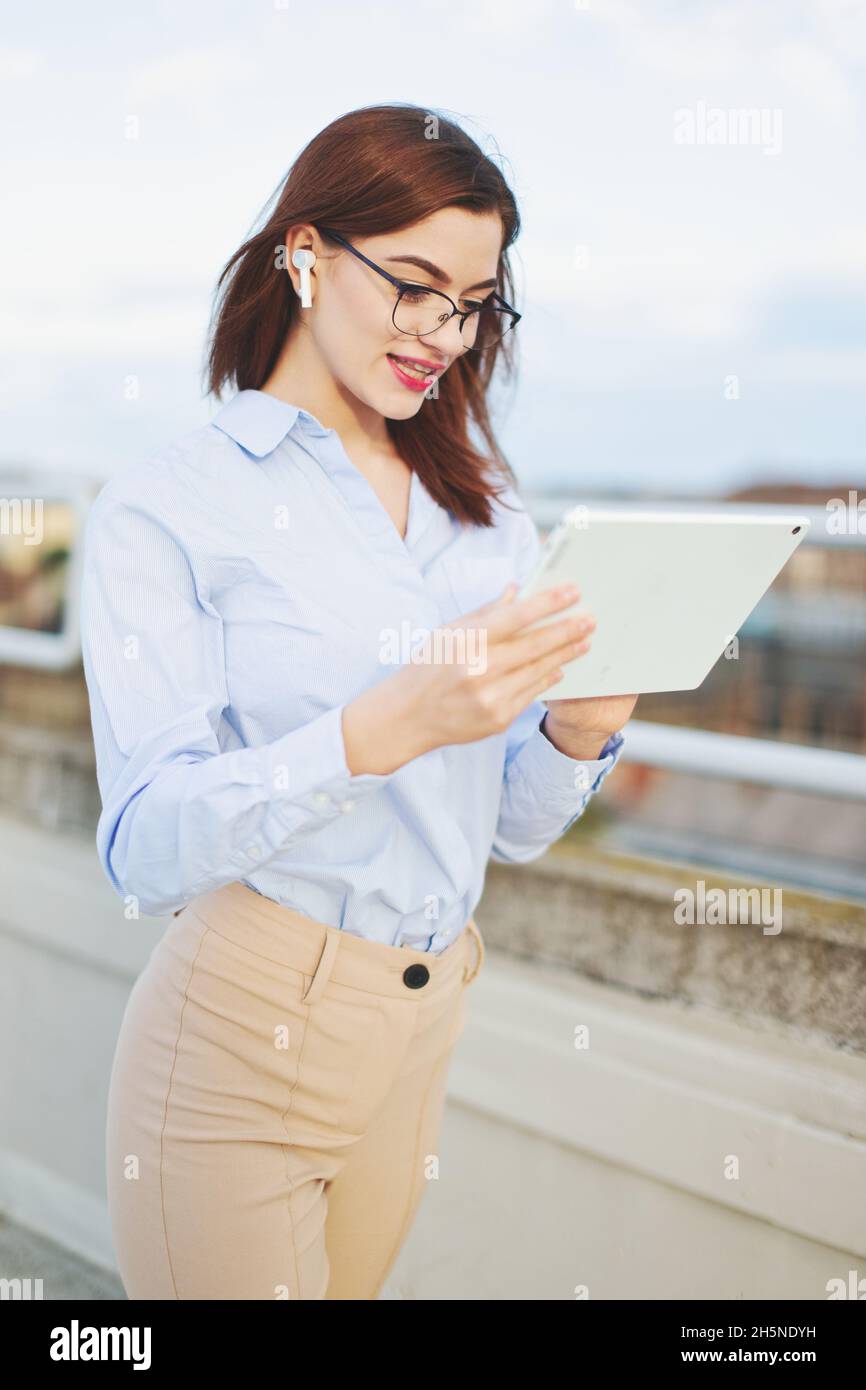 Redhead Caucasian young businesswoman with hands free device and tablet communicating outdoors Stock Photo