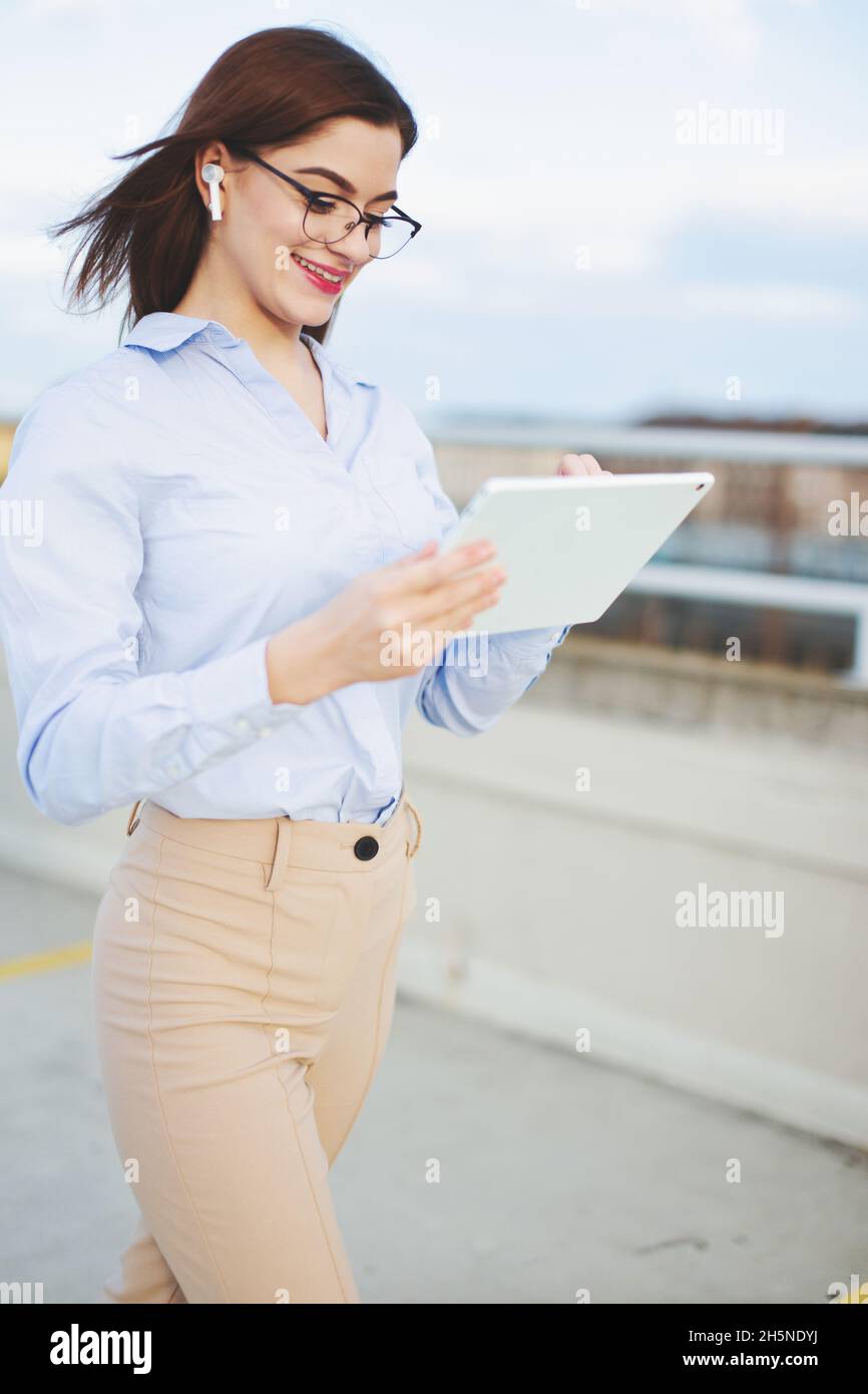 Redhead Caucasian young positive businesswoman with hands free device and tablet communicating outdoors Stock Photo