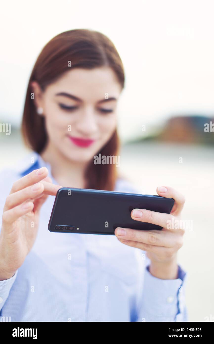 Young fresh redhead Caucasian businesswoman messaging on mobile phone outdoors, depth of field Stock Photo