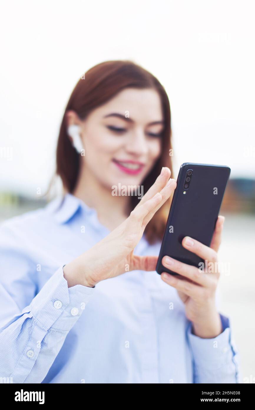 Young positive redhead Caucasian manager using smartphone outdoors, depth of field Stock Photo