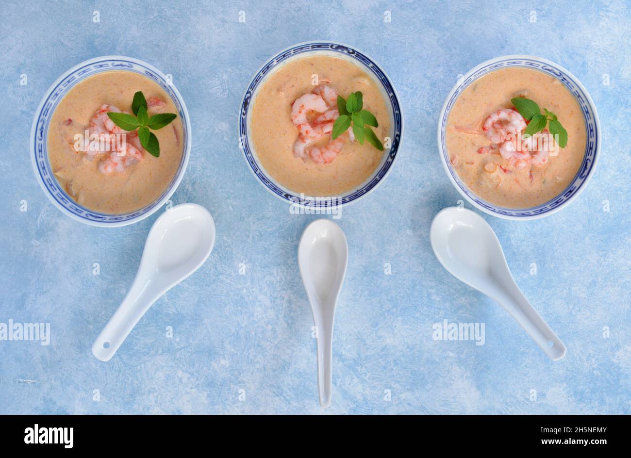 Spicy Thai red curry and coconut with prawns soup in traditional blue and white chinese bowls in horizontal format with thai basil garnish. Stock Photo