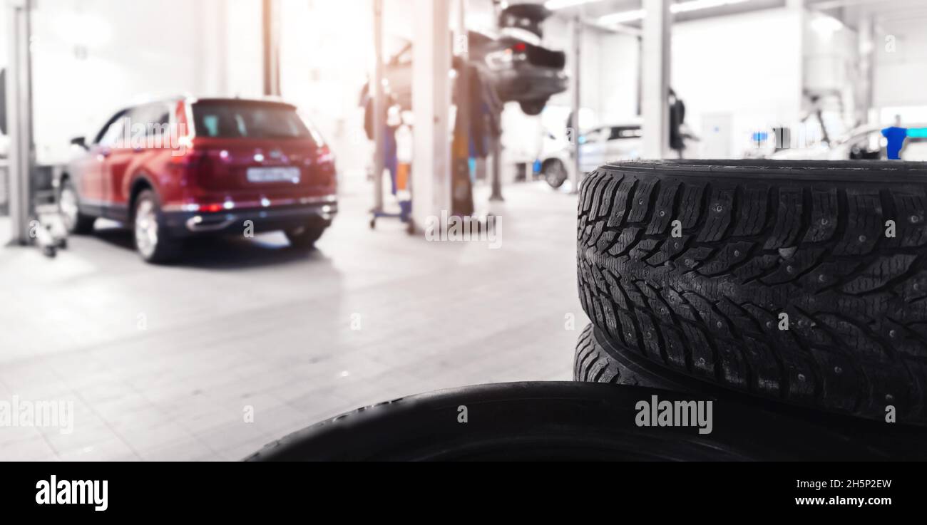 Banner winter tire with steel studs in car service, in background auto is lifted on lift. Stock Photo