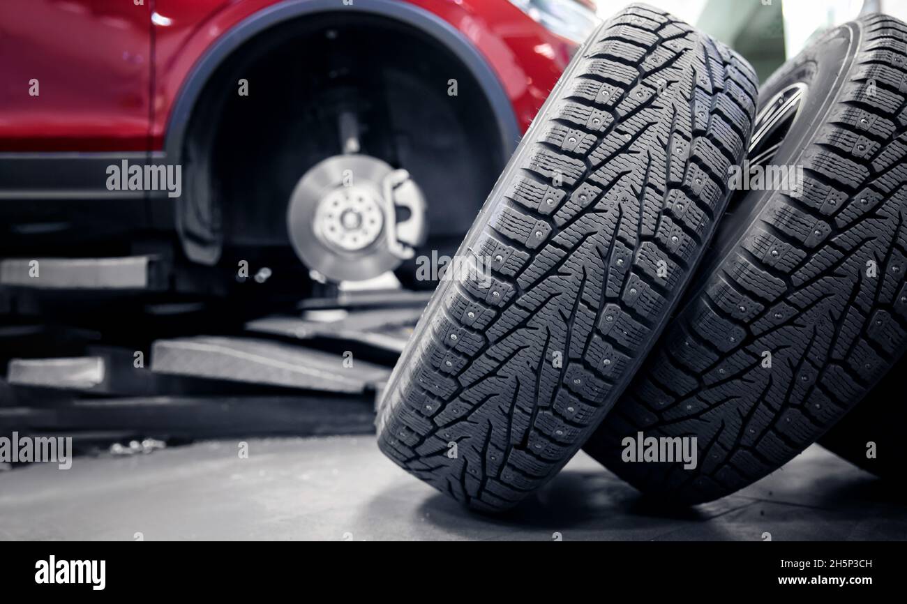 Selective focus winter tire with steel studs in service, in background car is lifted on lift. Stock Photo