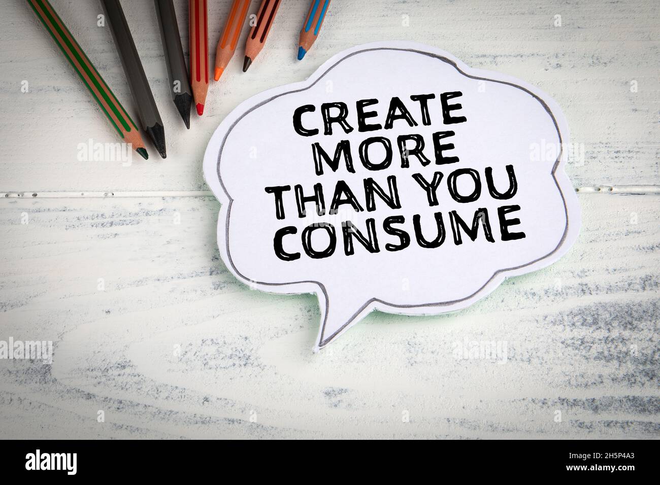 Create more than you consume. Speech bubble on a white painted wooden