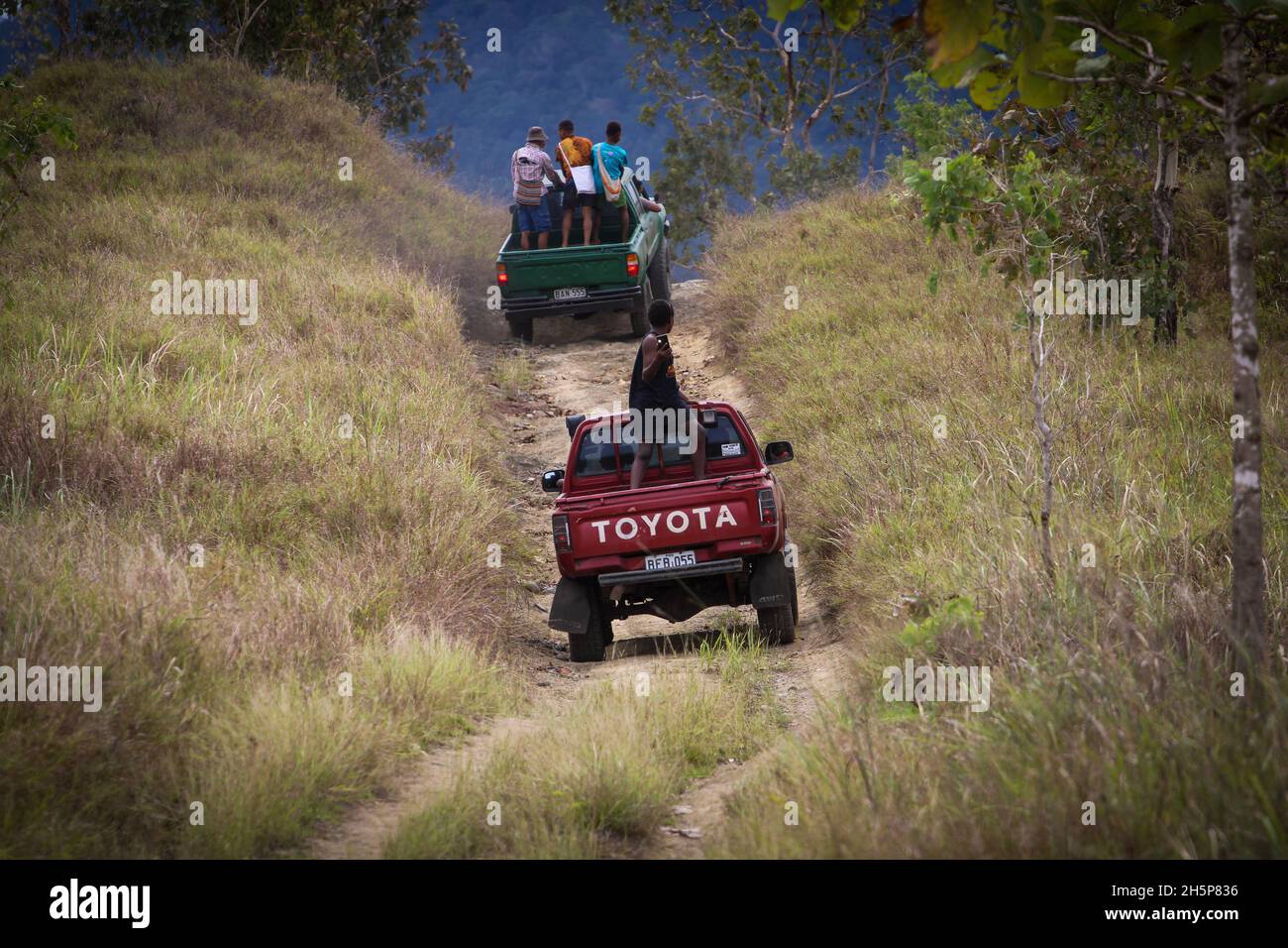 A couple of old model Toyota Hilux trucks going up a hill on an offroad track in Central Province, Papua New Guinea Stock Photo