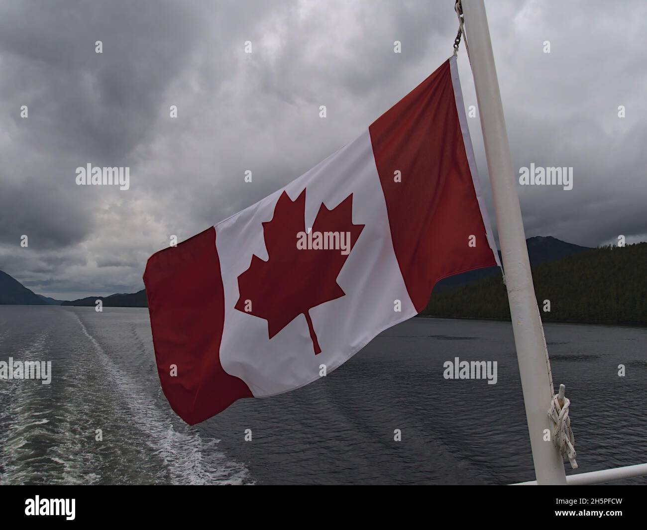 Red and white colored Canadian national flag with maple leaf flying in the wind at the stearn of a ferry boat crossing the Inside Passage, Canada. Stock Photo