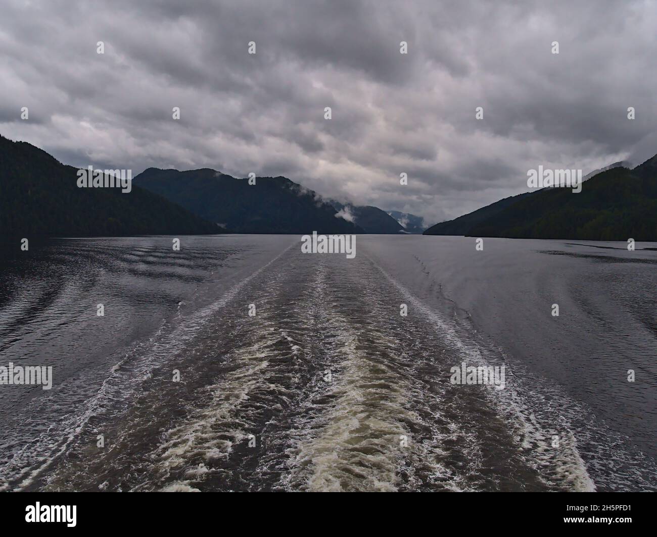 Beautiful stern view from ferry boat crossing the Inside Passage at Princess Royal Island, British Columbia, Canada with wake in the sea and mountains. Stock Photo