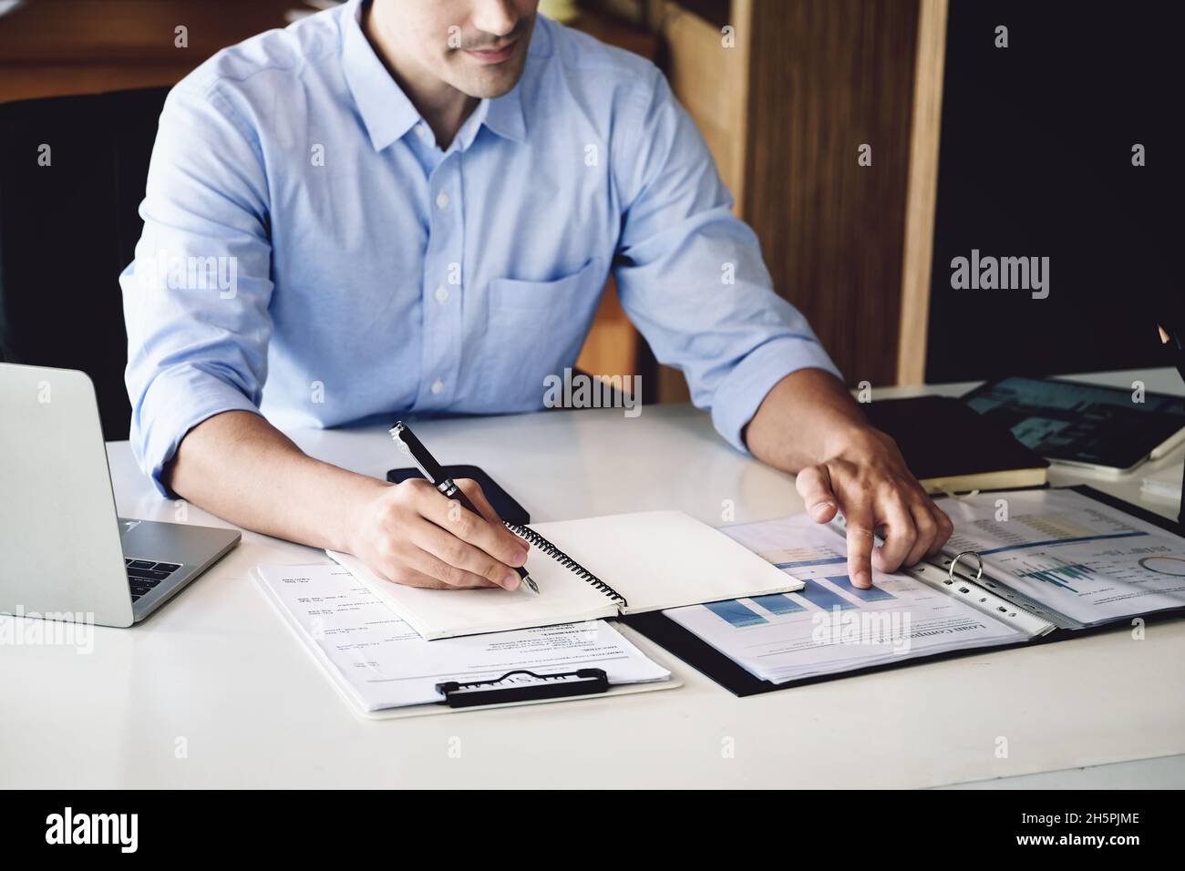 financial budget audit A male auditor is using a pen to write down budgets to trace the company's financial fraud. Stock Photo