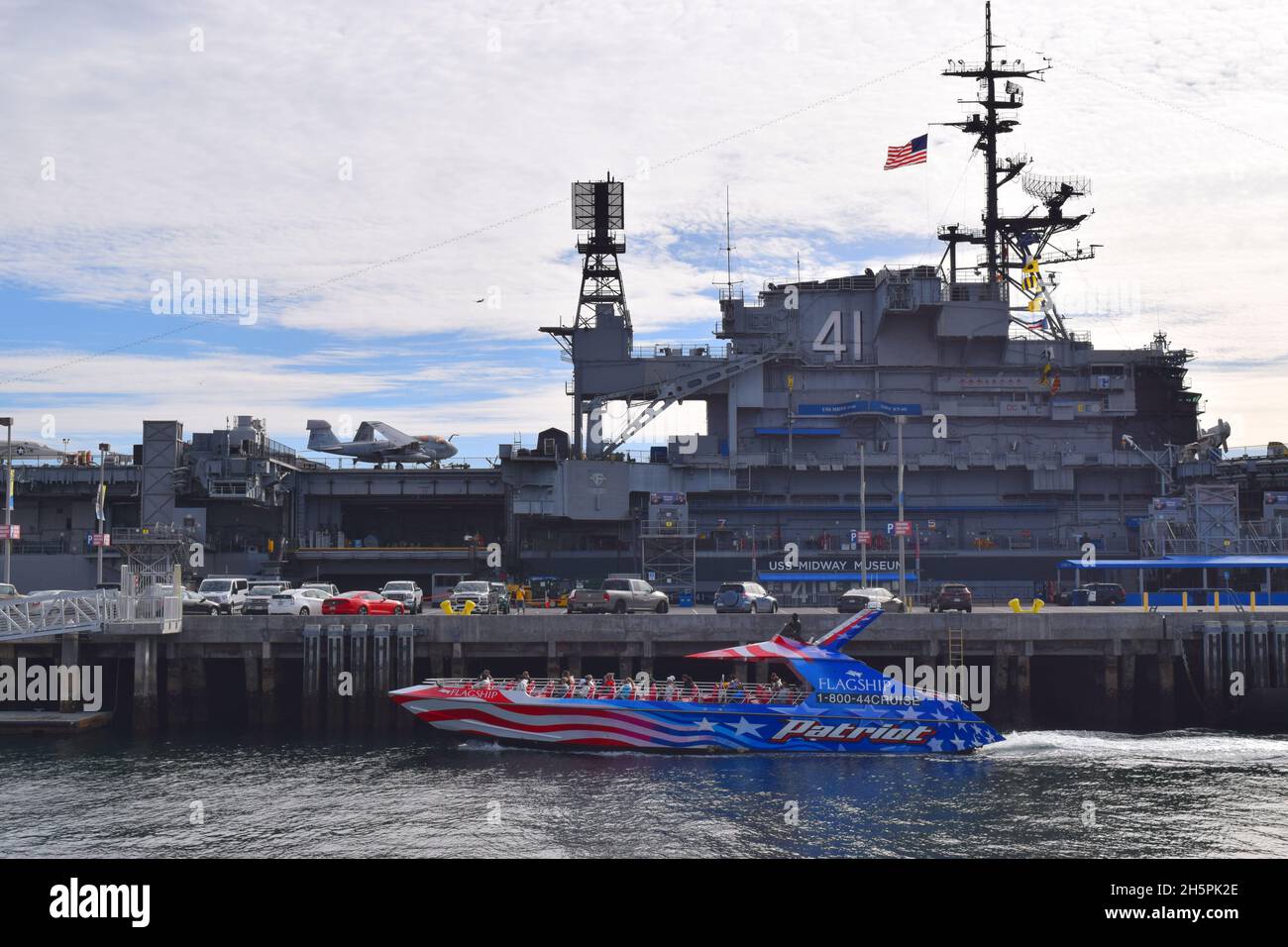 View of USS Midway, which served in WWII; now a museum ship moored in San Diego, California.  Tourist boat in the foreground.  Tower in the background Stock Photo