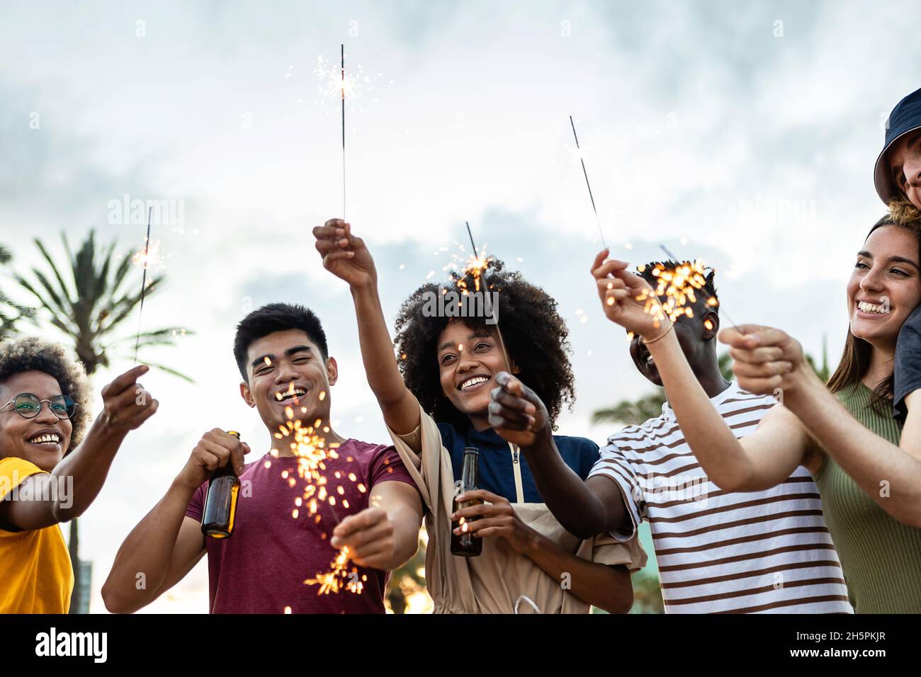 Group of multiracial friends laughing and celebrating with sparkles outdoors Stock Photo