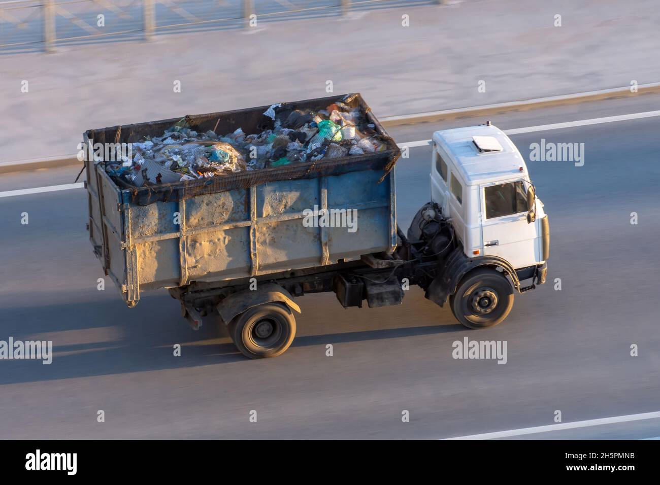 Truck with a metal container full of garbage goes down the highway to the dump Stock Photo